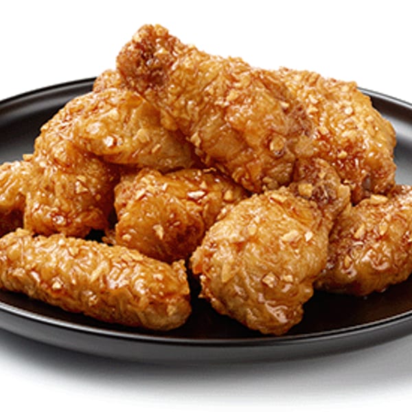 Golden-brown glazed fried chicken pieces with visible nuts on a black plate.