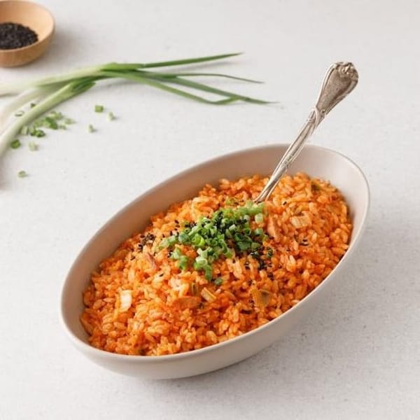 Vibrant orange kimchi fried rice in an oval bowl, garnished with green onions and sesame seeds.