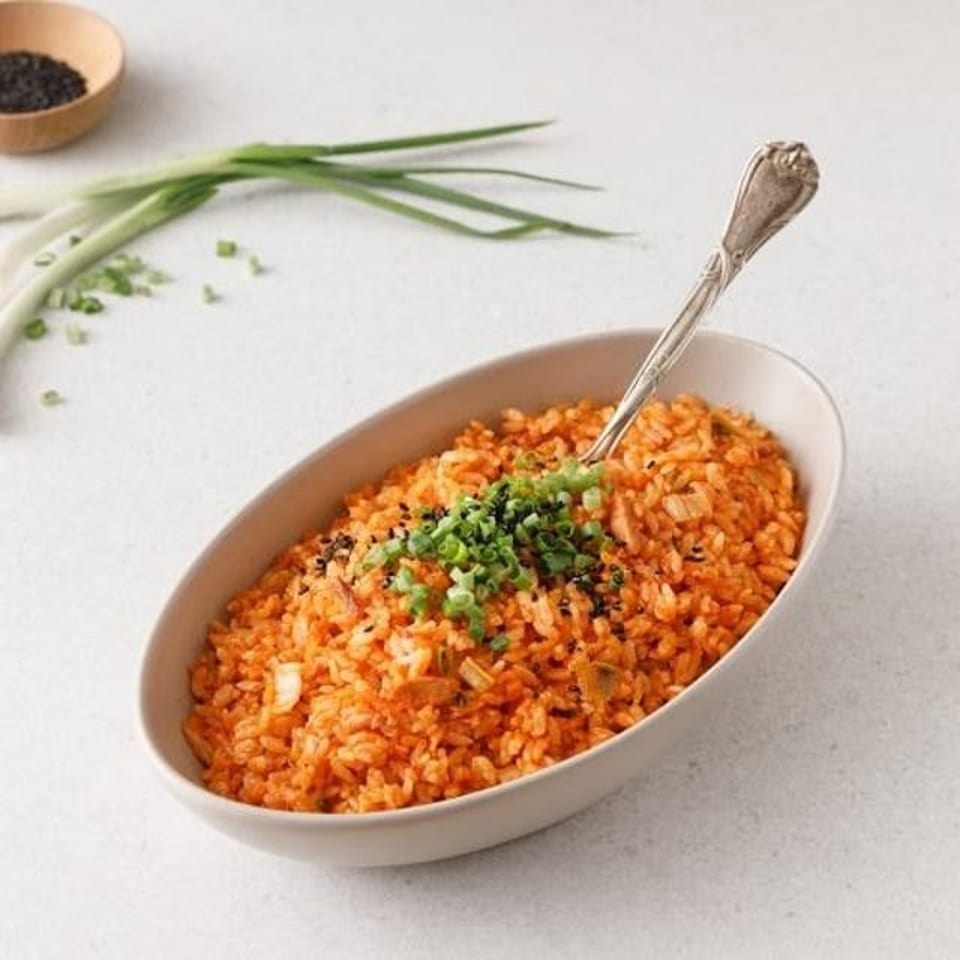 Vibrant orange kimchi fried rice in an oval bowl, garnished with green onions and sesame seeds.