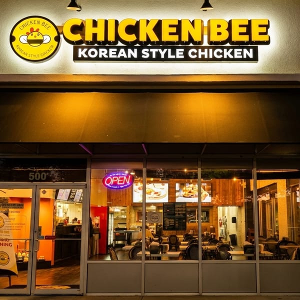 Exterior of Chicken Bee Korean Style Chicken restaurant at night, with illuminated sign and interior visible.